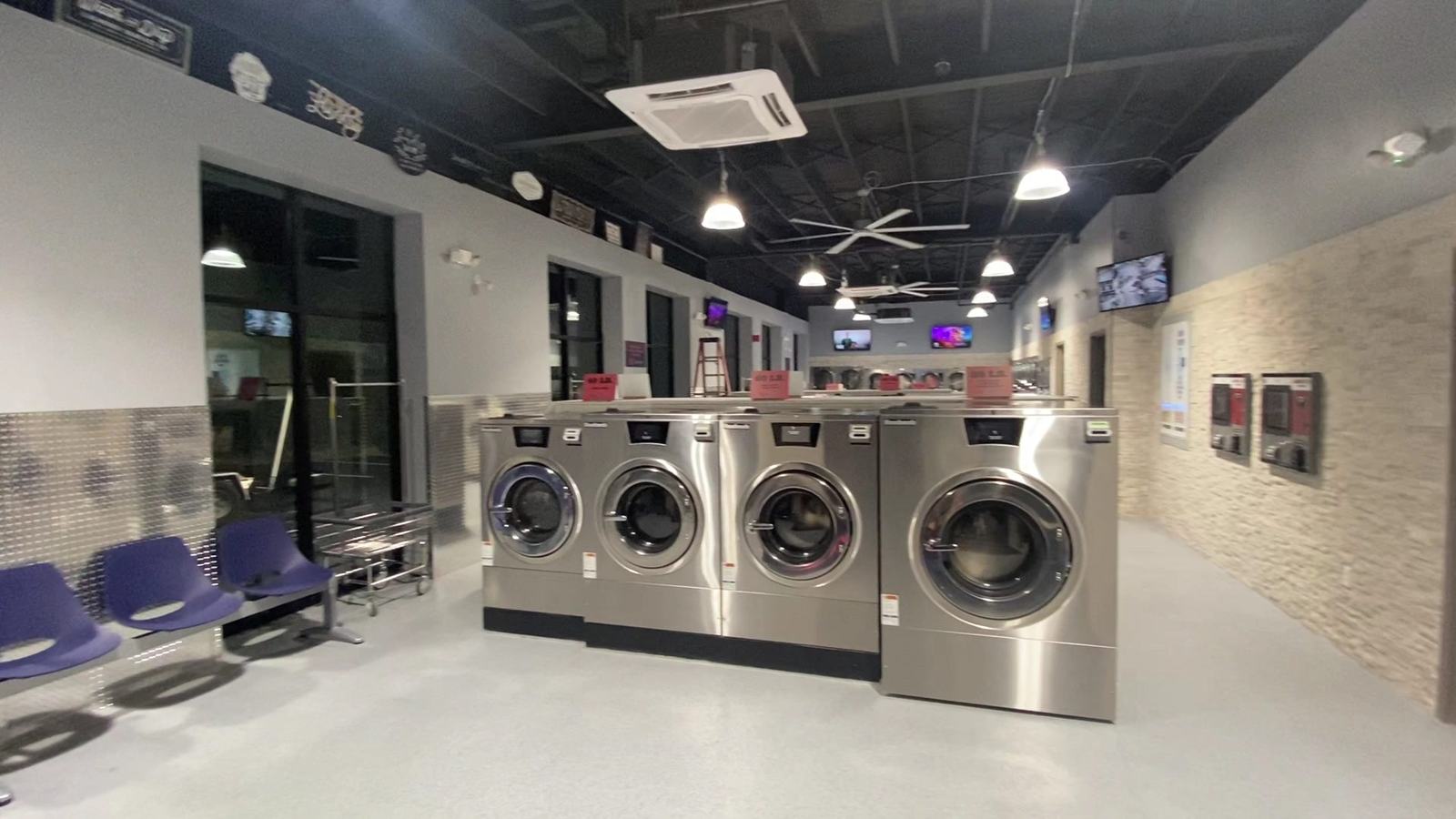 Bright interior of TLC Laundry showing rows of stainless steel washers and seating