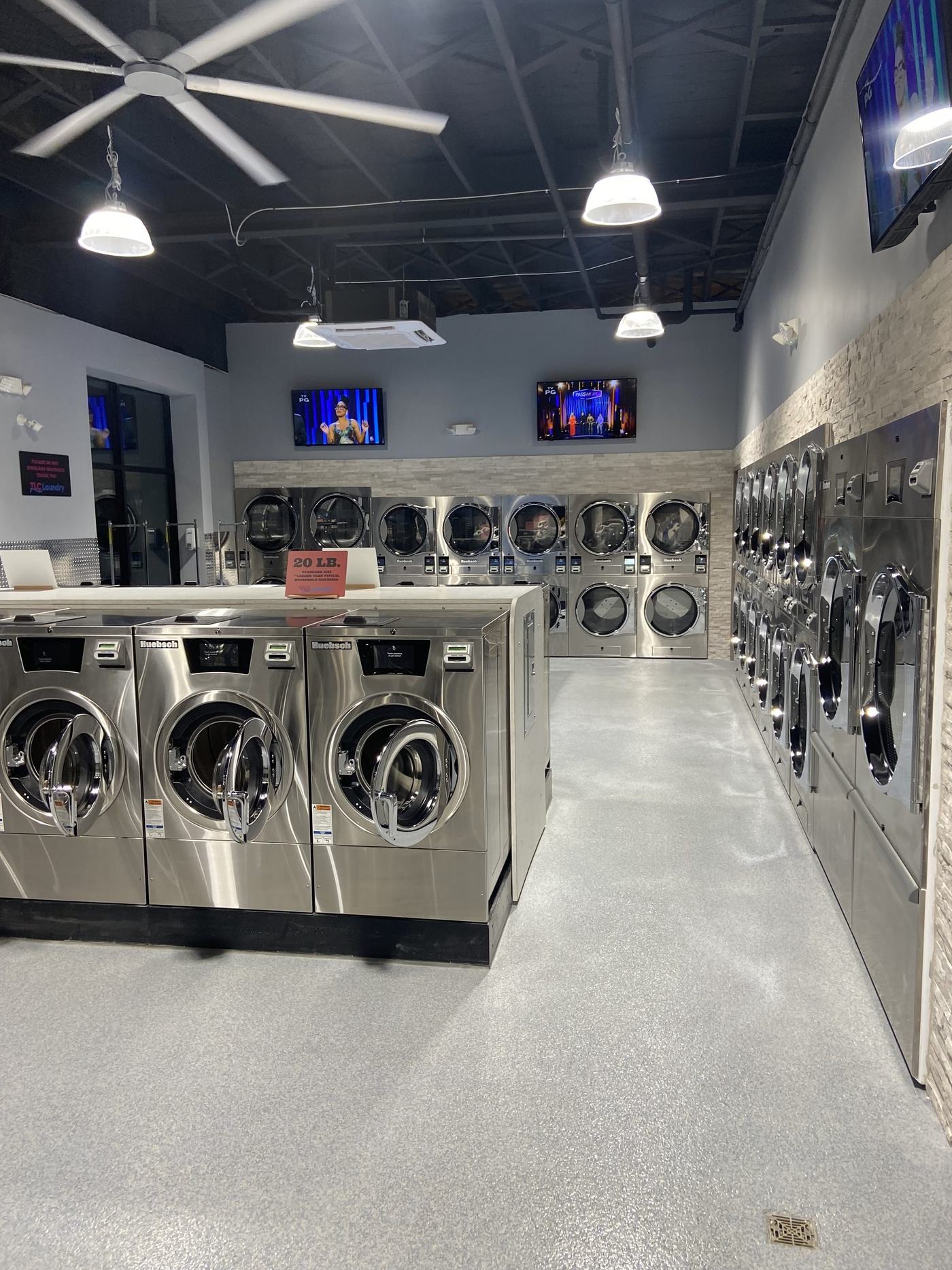 Aisle of washers and dryers at TLC Laundry with televisions and ceiling fans