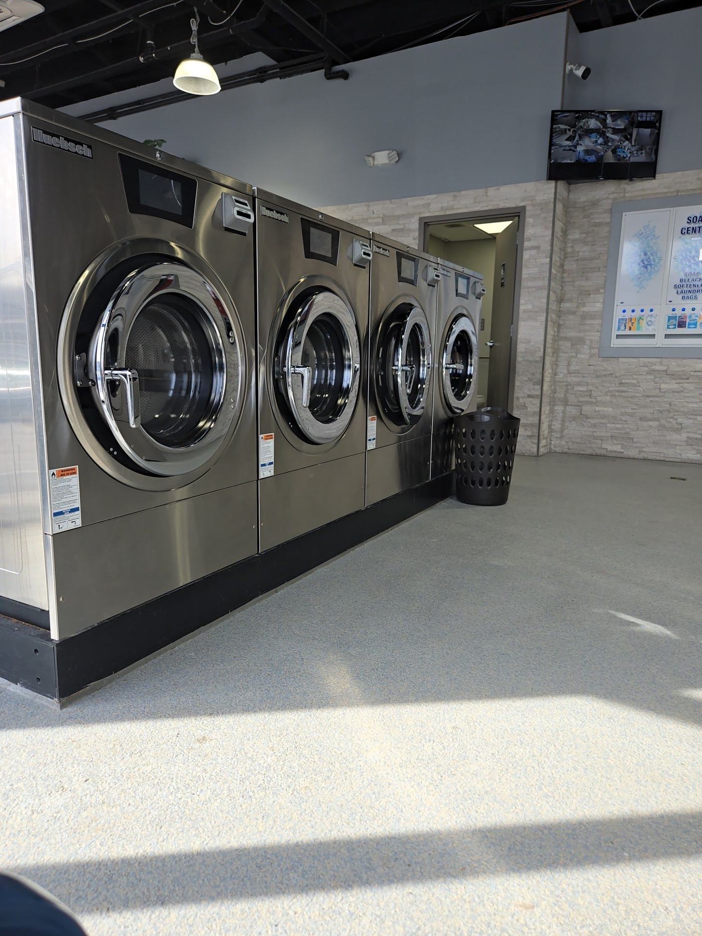 A row of stainless steel front-load washing machines at TLC Laundry in Towson